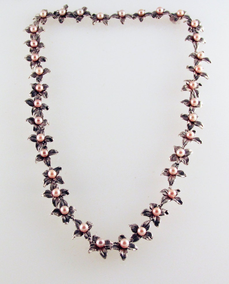 May include: A silver necklace with a delicate floral design and pink pearls. Each flower is accented with a single pearl, creating a feminine and elegant look.