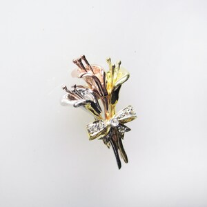 May include: A gold, silver, and rose gold brooch featuring a bouquet of stylized calla lilies with a diamond-encrusted bow.