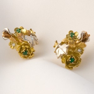 May include: A pair of gold earrings with a floral design. The earrings feature green and white gemstones and leaves.
