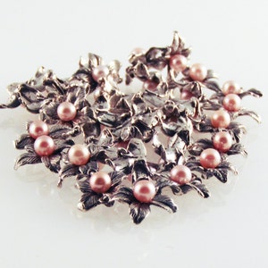 May include: A silver brooch with a floral design and pink pearls. The brooch is made of intricate metalwork and features a cluster of pearls in the center.
