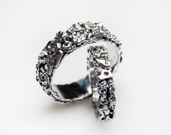 May include: Two silver rings with intricate designs, one ring is stacked on top of the other. The rings are made of silver and have a textured surface.