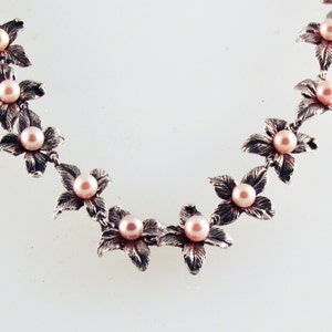 May include: A silver necklace with delicate flower charms and pink pearls.