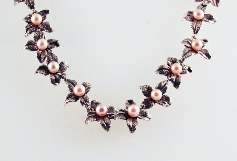 May include: A silver necklace with delicate flower charms and pink pearls.