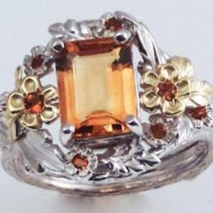 May include: A gold and silver ring with an orange gemstone surrounded by small red gemstones and floral designs.