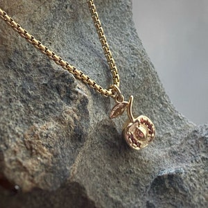 May include: A gold chain necklace with a small gold cherry pendant. The cherry has a textured surface and a small leaf.