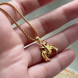 May include: A gold chain necklace with a pendant shaped like two bats facing each other.