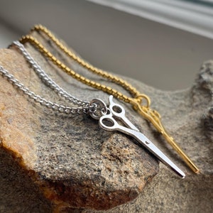 May include: Two silver necklaces with a silver scissor pendant. The necklaces are on a rock.