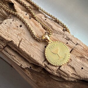 May include: A gold chain necklace with a round pendant featuring a chalice and the words "Holy Communion".