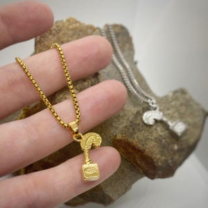 May include: A gold chain necklace with a small gold pendant shaped like a bottle of perfume with a feather on top.