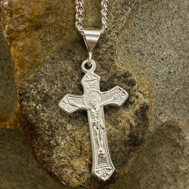 May include: A silver chain necklace with a silver crucifix pendant. The crucifix features a detailed depiction of Jesus Christ.