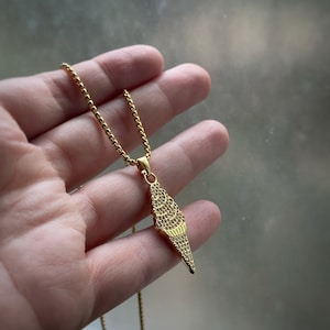 May include: A gold chain necklace with a gold ice cream cone pendant. The pendant is covered in small, sparkling stones.