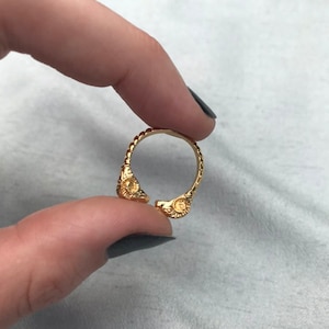 Może przedstawiać: Złoty pierścionek z fakturowanym wzorem i dwoma okrągłymi akcentami. Pierścionek jest otwarty z jednej strony.