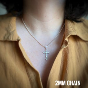 May include: A silver chain necklace with a silver crucifix pendant. The chain is 2mm thick.