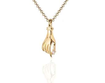 Könnte beinhalten: Eine goldene Halskette mit einem Anhänger in Form einer Hand, die einen kleinen Diamanten hält. Die Halskette liegt auf einem weißen Hintergrund.