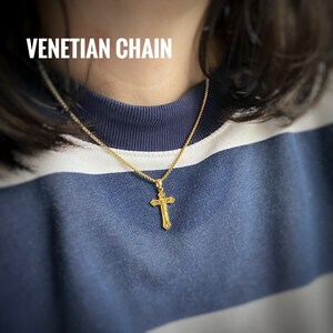 Pu&ograve; includere: Una collana a catena veneziana dorata con un ciondolo a croce dorato. La catena &egrave; sottile e delicata, e la croce &egrave; semplice ed elegante.