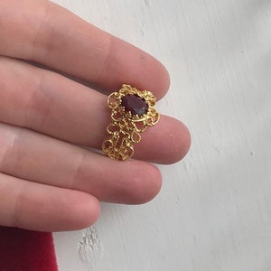 May include: A gold filigree ring with a dark red gemstone in the centre.