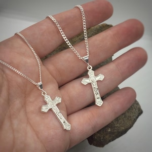May include: Two silver chains with silver crucifix pendants. The crucifixes have detailed engravings and feature a figure of Jesus Christ.