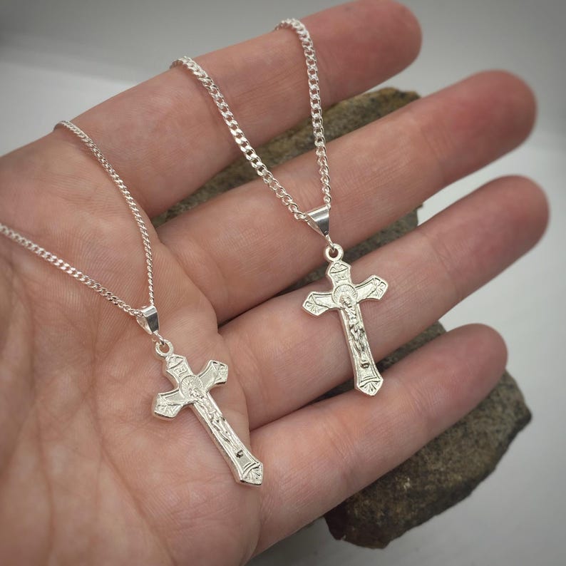 May include: Two silver chains with silver crucifix pendants. The crucifixes have detailed engravings and feature a figure of Jesus Christ.