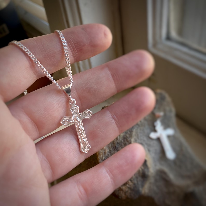 May include: A silver chain necklace with a silver crucifix pendant. The crucifix features a detailed depiction of Jesus Christ.