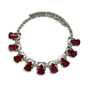 May include: A silver chain necklace with red glass teardrop-shaped beads. The beads are attached to silver square-shaped charms.
