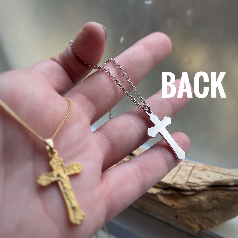 Pu&ograve; includere: Due collane d'argento con croci, una con un ciondolo a croce d'oro e l'altra con un ciondolo a croce d'argento. La parola "BACK" &egrave; scritta sul retro della mano che tiene le collane.