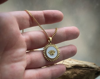 May include: Gold chain necklace with a white circular pendant featuring a gold evil eye design.