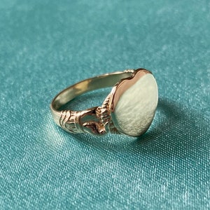 May include: A gold signet ring with a heart-shaped top. The ring has a detailed design on the band.