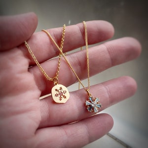 K&ouml;nnte beinhalten: Zwei goldene Halsketten mit Schneeflockenanh&auml;ngern. Ein Anh&auml;nger ist eine massive goldene Schneeflocke, der andere ist eine Schneeflocke mit klaren Kristallen.