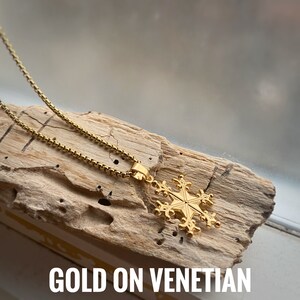 May include: Gold snowflake pendant necklace on a gold Venetian chain. The necklace is displayed on a piece of driftwood.
