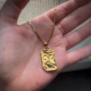Pu&ograve; includere: Una collana con catena dorata con un ciondolo dorato che presenta il simbolo astrologico dell'Ariete. Il ciondolo &egrave; di forma rettangolare e testurizzato.