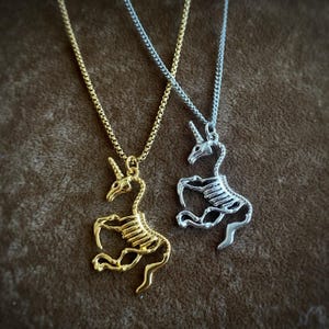 Op de afbeelding: Twee kettingen met een skelet-eenhoorn hanger. De ene ketting is goud en de andere is zilver.