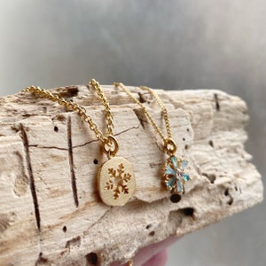 K&ouml;nnte beinhalten: Zwei goldene Halsketten mit Schneeflockenanh&auml;ngern. Ein Anh&auml;nger ist eine massive goldene Schneeflocke, der andere ist eine Schneeflocke aus blauen Kristallen.