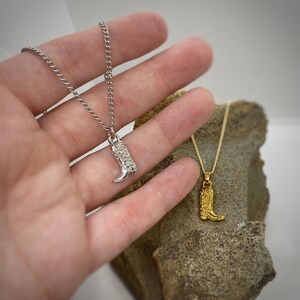 Puede incluir: Dos collares de plata y oro con un colgante de bota. El collar de plata tiene un colgante de bota de plata con una superficie texturizada. El collar de oro tiene un colgante de bota de oro con una superficie texturizada.