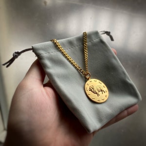 May include: A gold chain necklace with a round pendant featuring a detailed image of a ram. The pendant is surrounded by zodiac symbols.
