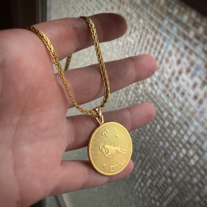 May include: A gold chain necklace with a round pendant featuring the zodiac sign Aries. The pendant is engraved with the word "Aries" and has a star design.