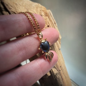 Könnte beinhalten: Eine goldene Kettenkette mit einem herzförmigen Anhänger. Der Anhänger ist aus dunkelblauem Glas und hat ein goldenes Filigranmuster.