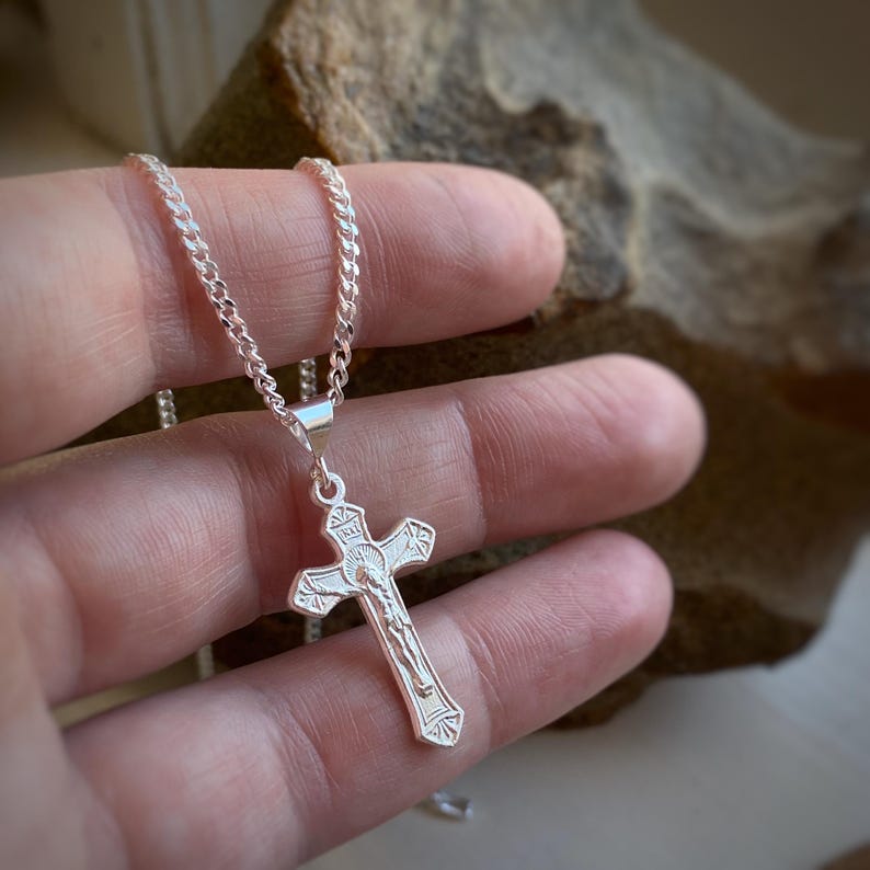 May include: A silver chain necklace with a silver crucifix pendant. The crucifix features a detailed image of Jesus Christ.