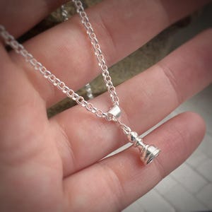 Op de afbeelding: Een zilverkleurige ketting met een schaakstuk hanger. De hanger is een gedetailleerde miniatuur van een schaakstuk, hangend aan een delicate ketting. De ketting en hanger zijn gemaakt van een glanzend, reflecterend metaal.