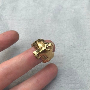 May include: A gold-colored ring featuring a detailed bird design. The bird is depicted with its wings spread, as if in flight.