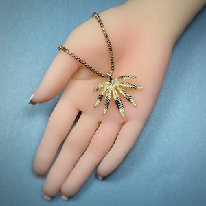 May include: A gold chain necklace with a large, detailed, gold marijuana leaf pendant.