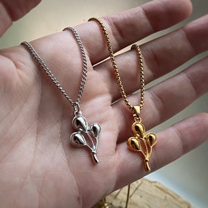 May include: Two silver and gold necklaces with a cluster of balloon charms. The charms are shaped like a bunch of balloons tied together.