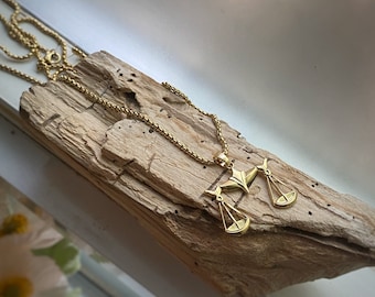 May include: A gold chain necklace with a pendant featuring a stylized depiction of a scale of justice.