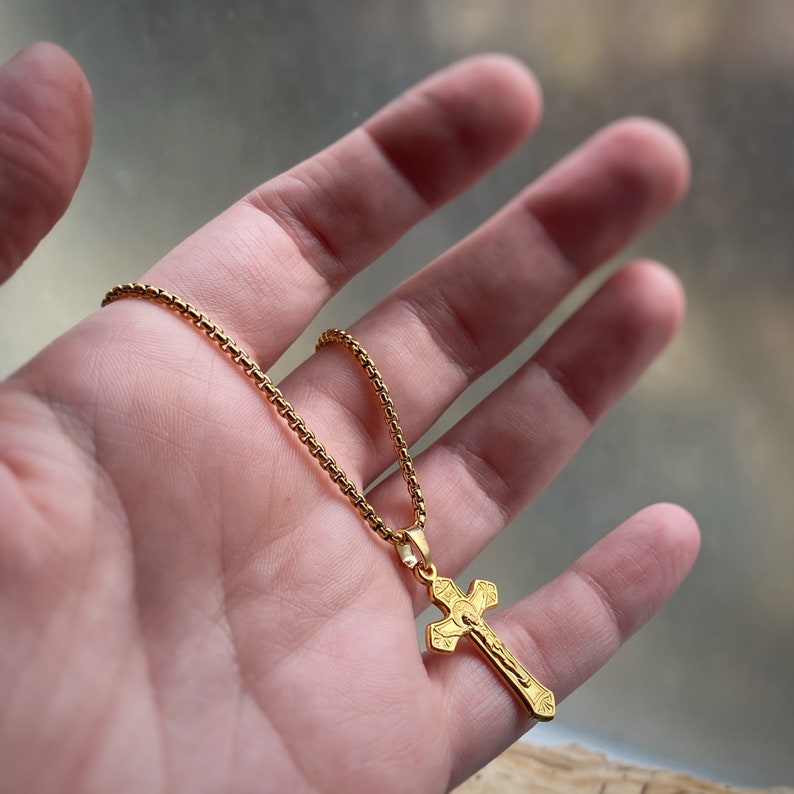 Pu&ograve; includere: Una collana con catena dorata e un ciondolo a forma di croce dorata. La croce ha un design dettagliato e presenta una figura di Ges&ugrave; Cristo.