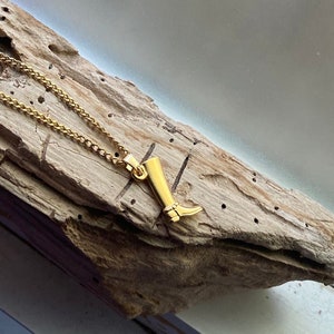 Könnte beinhalten: Eine goldene Kettenkette mit einem goldenen Anhänger in Form eines Stiefels. Der Stiefelanhänger ist detailliert und hat eine spitze Spitze.