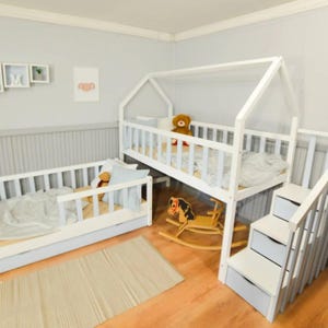 Puede incluir: Cama de madera blanca en forma de casa con una escalera incorporada y una segunda cama. Las camas tienen laterales de listones y están amuebladas con ropa de cama y animales de peluche. También hay un caballito balancín.