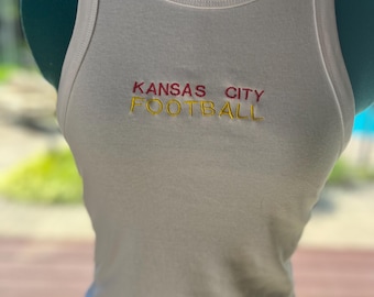 May include: White tank top with the words "Kansas City Football" embroidered in red and yellow.