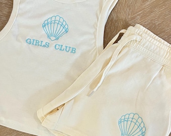 May include: A white tank top and matching shorts set with a blue embroidered seashell and the text "GIRLS CLUB".