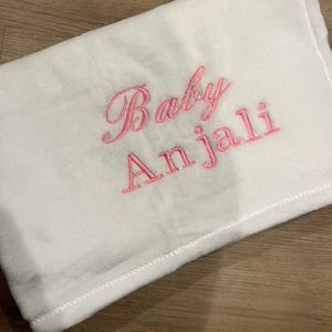 Puede incluir: Manta de bebé blanca con bordado rosa que dice "Baby Anjali".