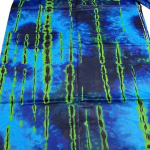 May include: A vibrant blue fabric with a pattern of vertical black and green streaks. The fabric has a tie-dye effect with swirling blue patterns. The fabric is folded and appears to be new.