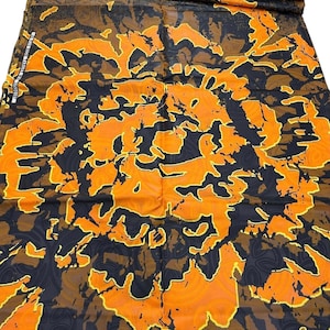 May include: A folded fabric with a vibrant abstract pattern. The design features large, irregular shapes in shades of orange, black, and brown, outlined with yellow. The fabric appears to be a medium weight, suitable for various sewing projects.